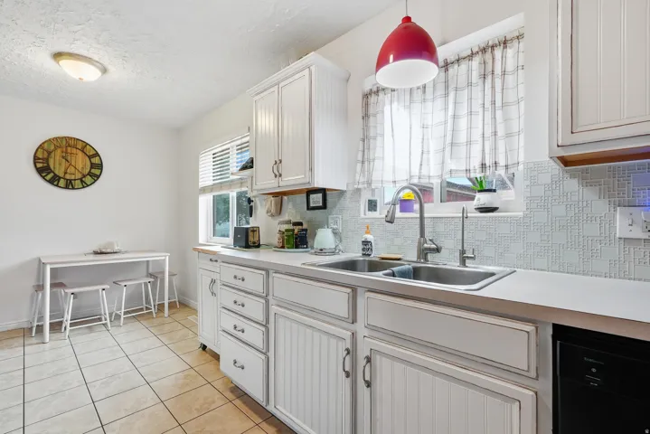 White cabinetry, light-toned countertops, stainless steel double-basin sink, patterned tile backsplash, and ceramic tile flooring