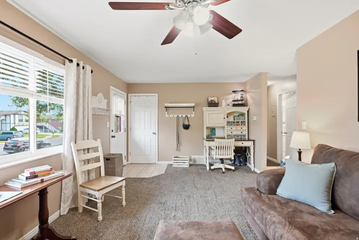 Living area featuring neutral wall tones, carpeted flooring, a ceiling fan, and a front entry door with ceramic tile