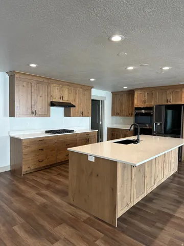 Kitchen featuring wood-finish cabinetry, light-toned countertops, recessed lighting, wood-finish flooring, and a central island with an undermount sink