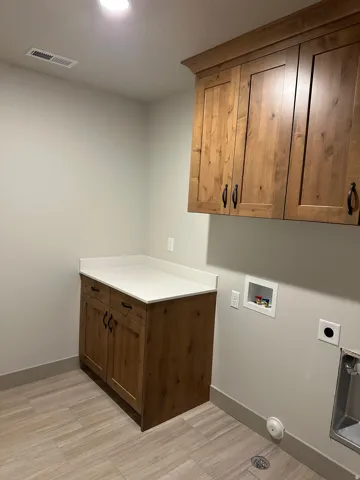 Wood-finish cabinetry with dark hardware, a light-toned countertop, and wood-finish tile flooring
