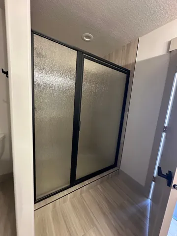 Frosted glass shower enclosure with black framing, recessed ceiling lighting, and wood-finish tile flooring
