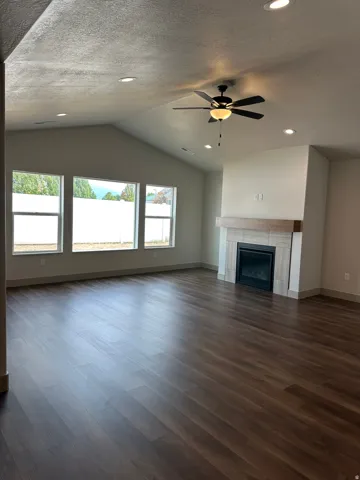 Vaulted ceiling with recessed lighting and ceiling fan, wood-finish flooring, three large windows, and a fireplace with a light wood mantel