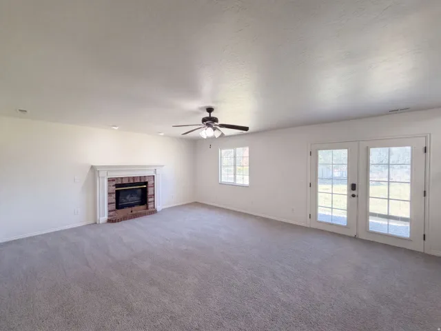 Spacious living area featuring neutral carpeting, a brick fireplace with a white mantel, recessed lighting, a ceiling fan, and French doors