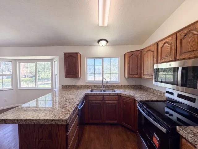 Kitchen featuring wood-finish cabinetry, stone-finish countertops, stainless steel microwave, black electric range, and a bay window