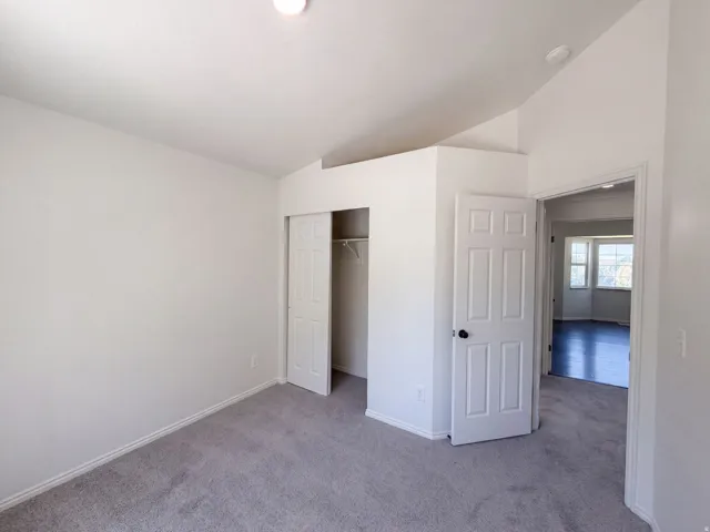 Carpeted flooring, vaulted ceiling, white walls, bi-fold closet doors, white paneled interior doors