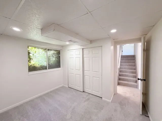 Recessed lighting, light-colored carpeting, white paneled bifold doors, window with exterior foliage, and a carpeted staircase