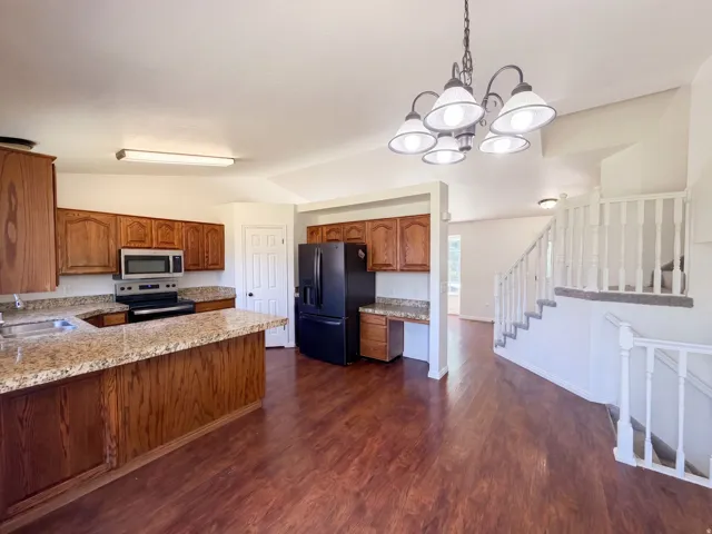 Kitchen with wood-finish flooring, wood cabinetry, stone countertops, and stainless steel appliances