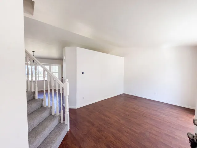 Wood-finish flooring, white painted walls, and carpeted stairs with a white banister