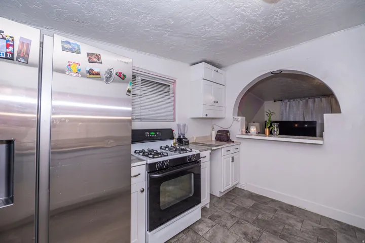 Stainless steel refrigerator, gas range, white cabinetry, tiled flooring, and an arched pass-through opening