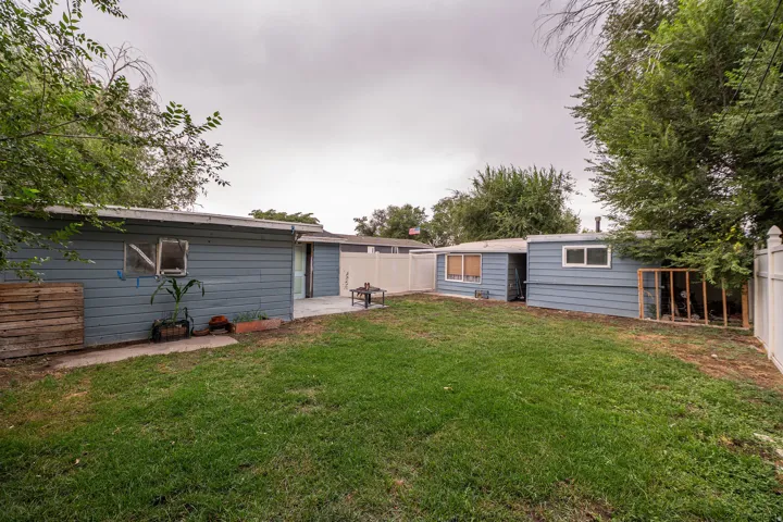 Expansive backyard featuring a green lawn, two detached structures with horizontal siding, a concrete patio, and white privacy fencing