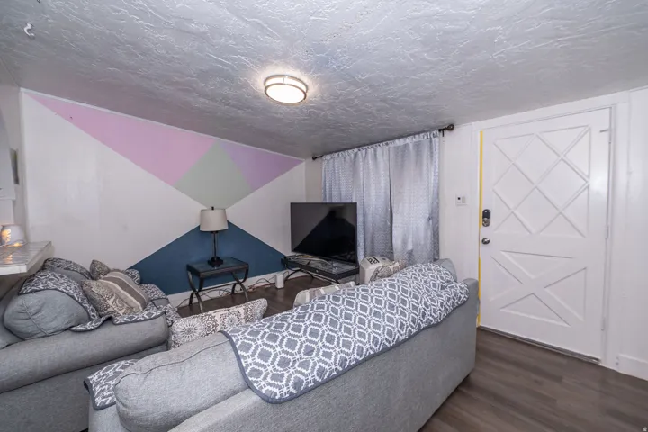 Sloped ceiling, patterned accent wall, dark wood-finish flooring, flush mount ceiling light, white paneled door