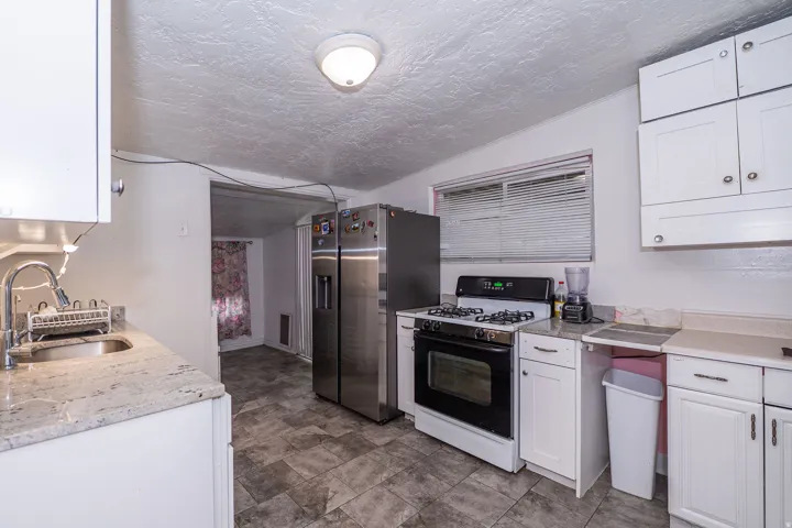 Kitchen featuring white cabinetry, light-toned countertops, a stainless steel sink with a gooseneck faucet, a gas range, and patterned floor tiles