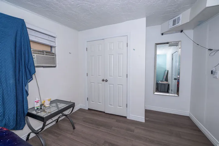 Wood-finish flooring with white baseboards, white bi-fold closet doors, and a window with blinds