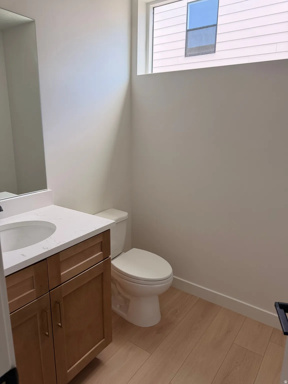 Wood-finish flooring, single vanity with a white countertop, recessed sink, and an integrated toilet