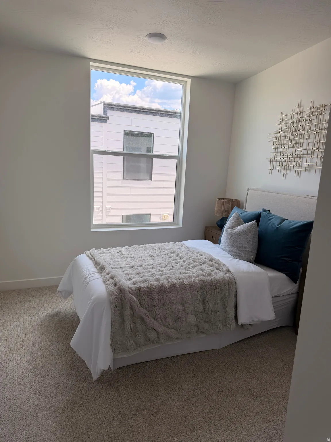 Recessed ceiling lighting, large window with white frame, light-toned carpet flooring, neutral wall finish, and a padded headboard