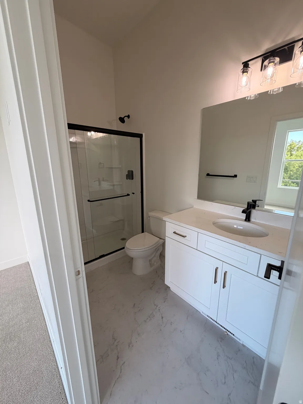 White shaker vanity with integrated sink, black fixtures, framed mirror, and glass-enclosed shower