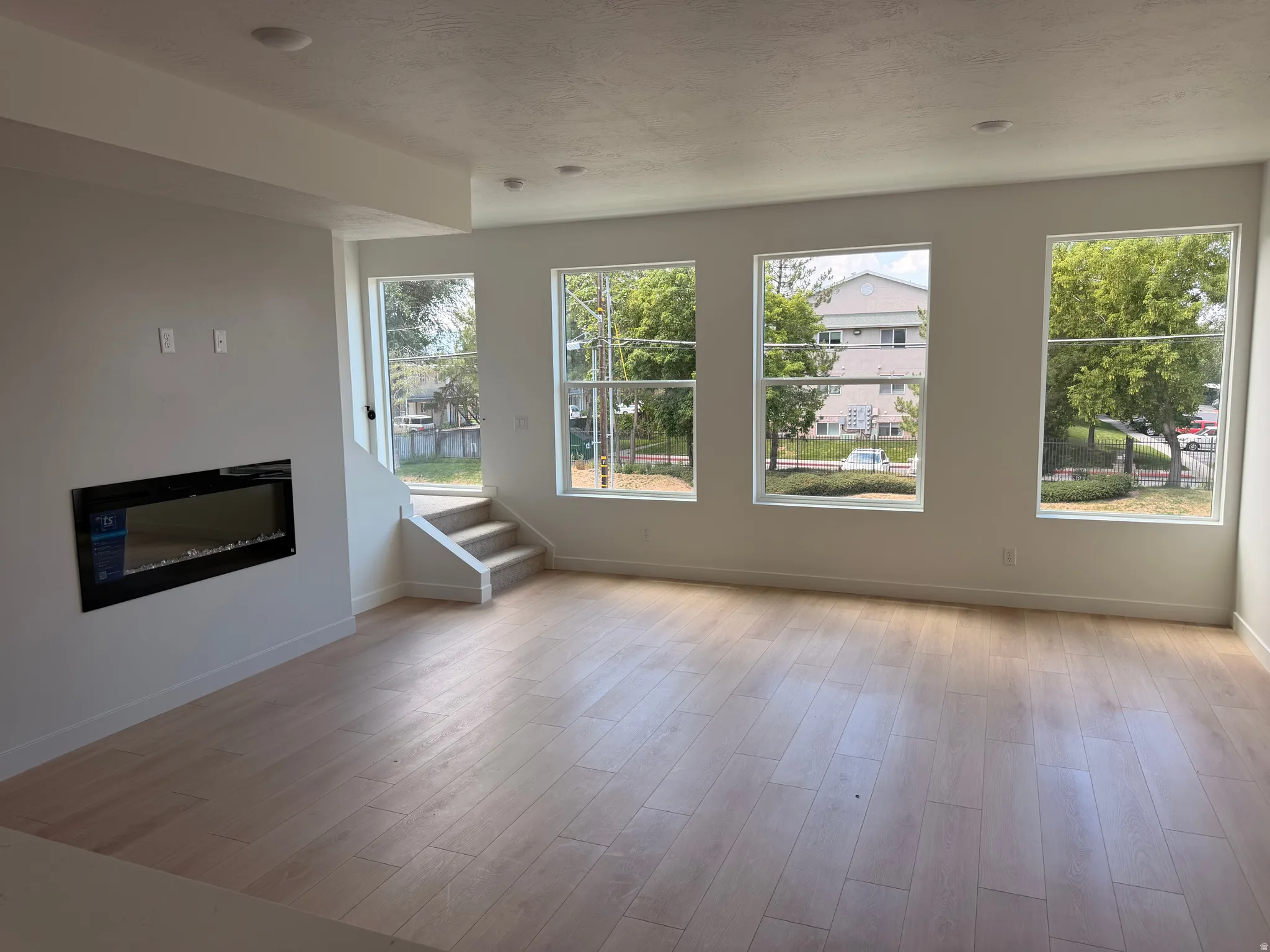 Recessed lighting, wood-finish flooring, built-in electric fireplace, multiple windows, and a carpeted stairway