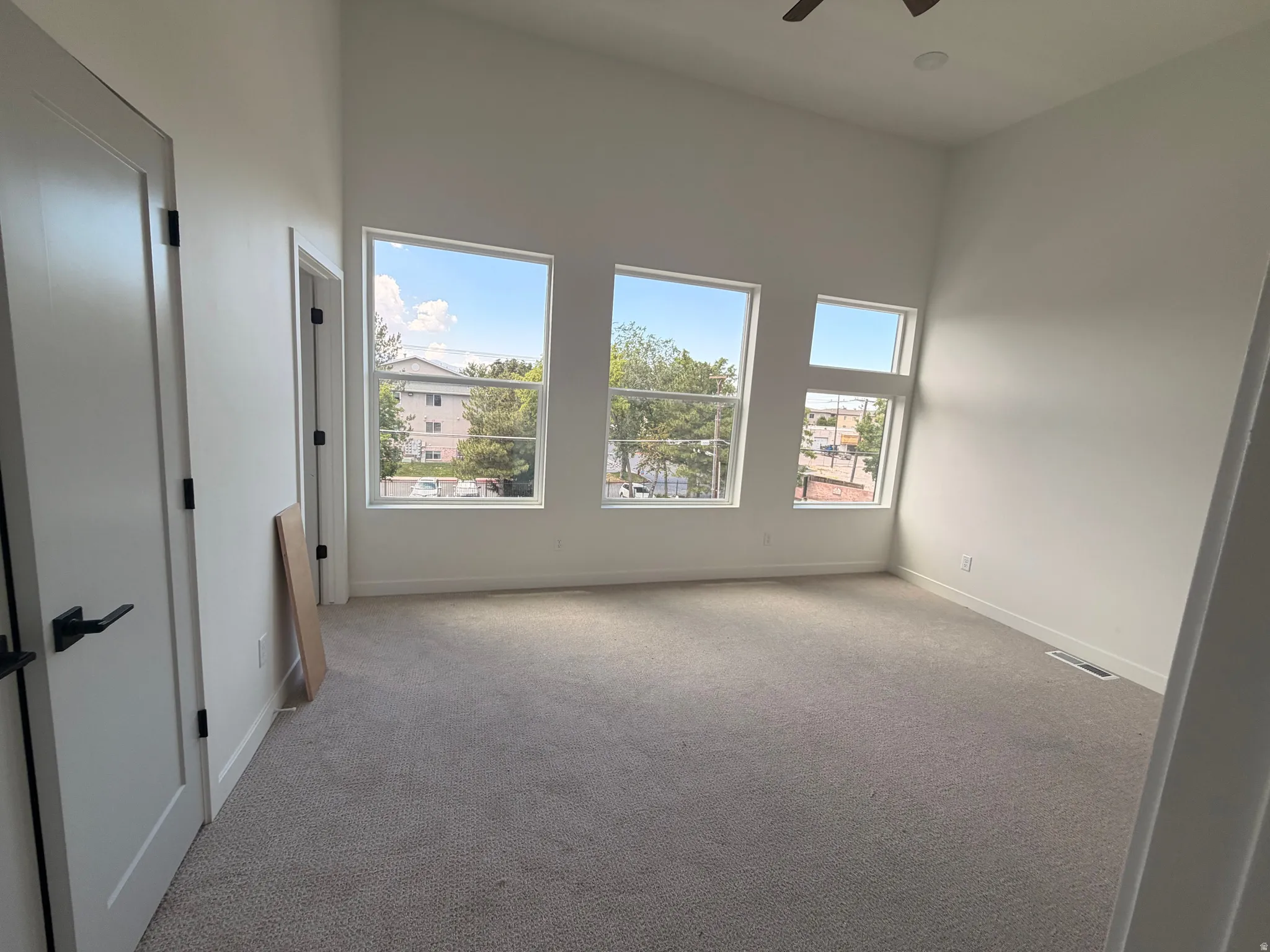 Vaulted ceiling with an integrated ceiling fan, multiple windows, light-toned carpeting, and a white interior door with black hardware