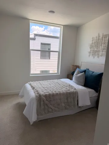 Recessed ceiling lighting, large window with white frame, light-toned carpet flooring, neutral wall finish, and a padded headboard