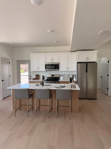 Central kitchen island with a white countertop and seating for three, complemented by stainless steel appliances, white cabinetry, and wood-finish flooring