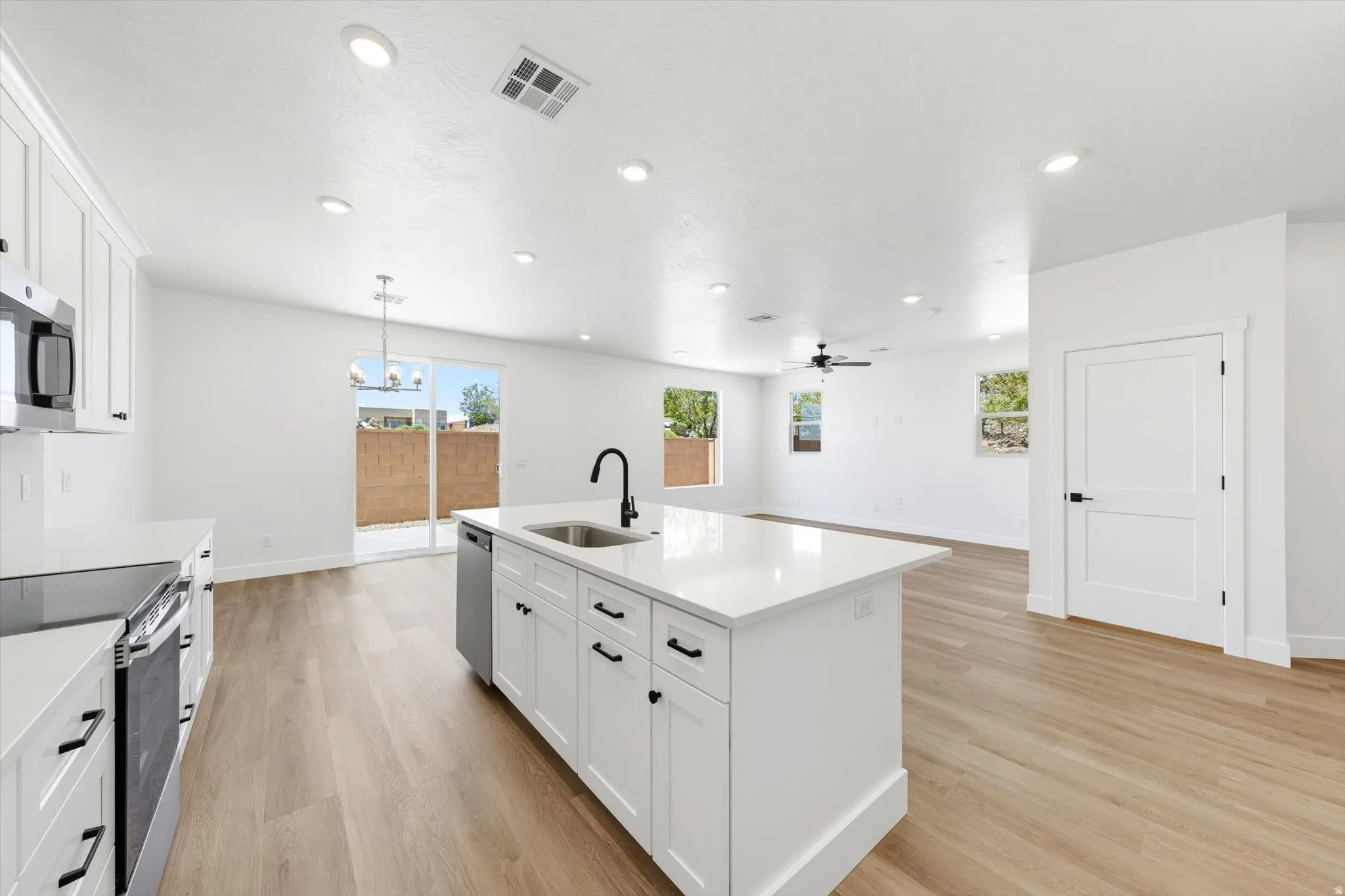 White kitchen cabinetry with black hardware, recessed lighting, wood-finish flooring, a kitchen island with an undermount sink, and sliding glass doors