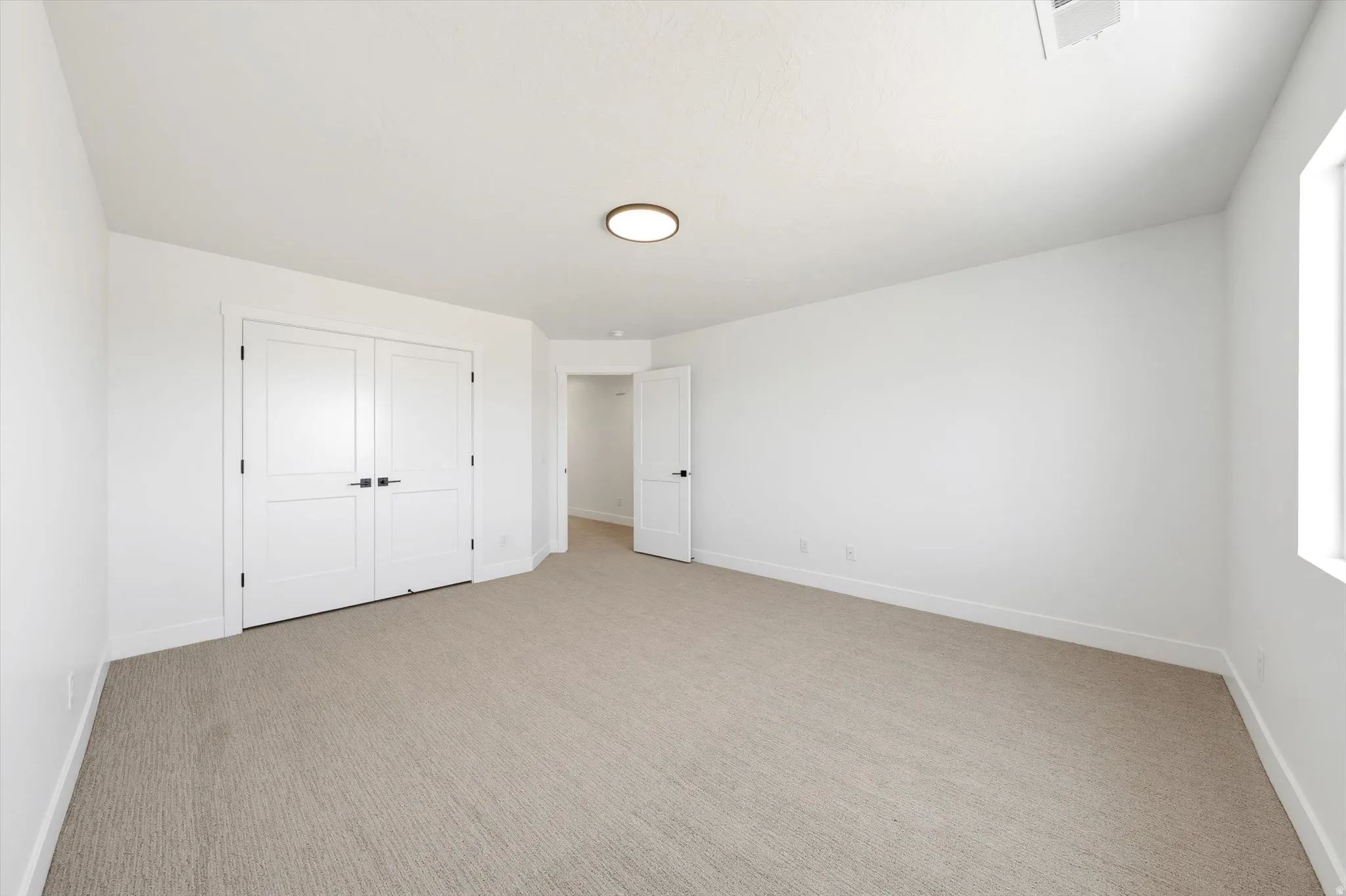 Neutral tone carpeting, white walls, and a flush-mount ceiling light fixture