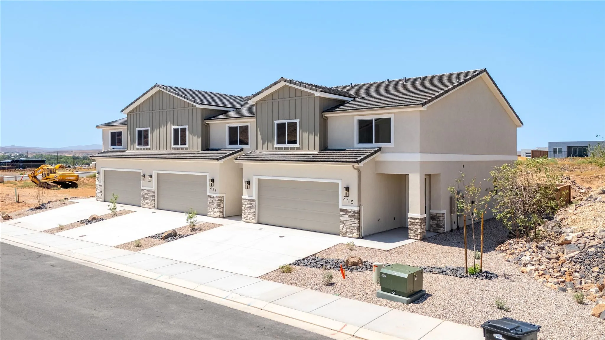 Contemporary townhome exterior featuring stucco and vertical siding, a dark shingle roof, stone accents, attached garages, and a paved driveway
