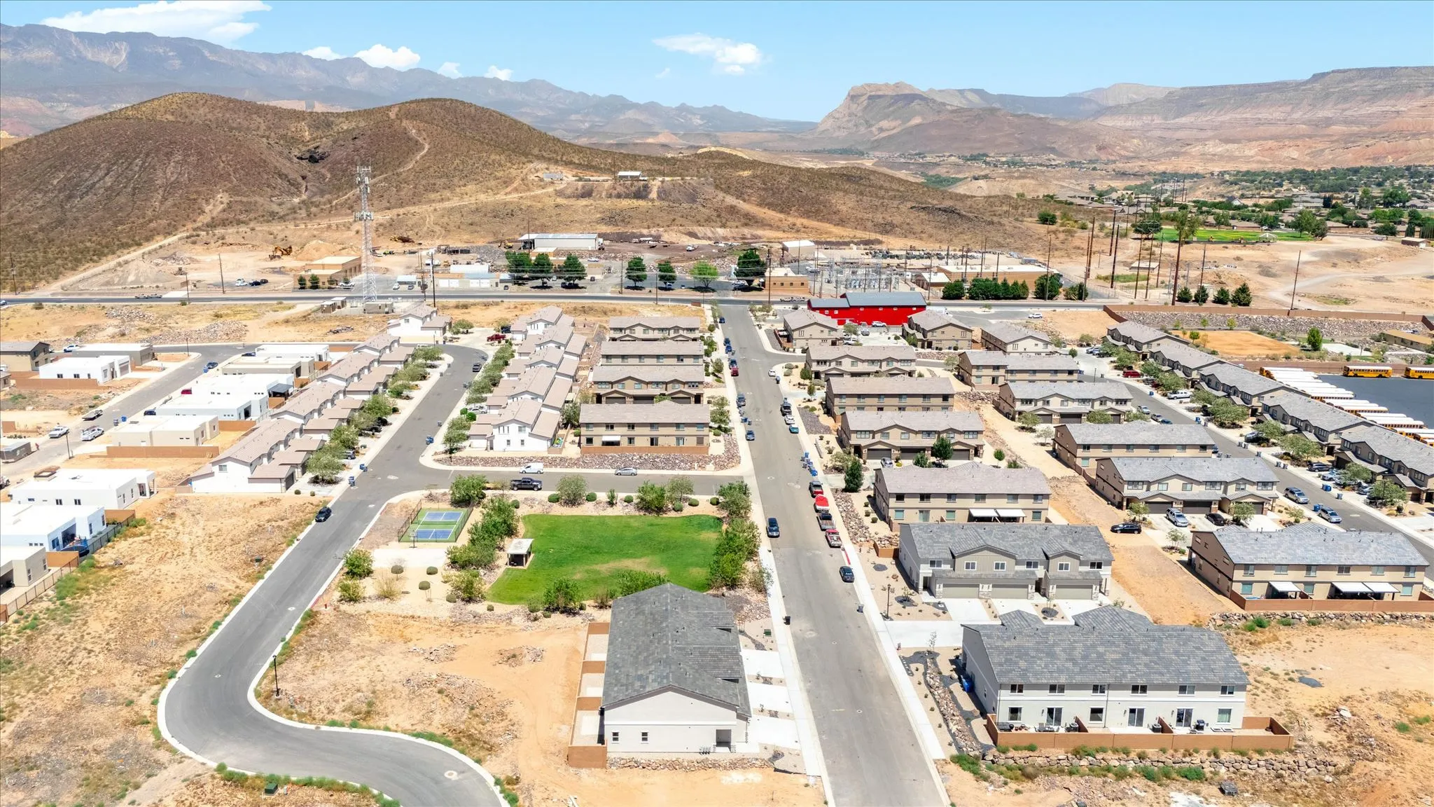 Community setting featuring a paved road network, uniform residential structures, a central green space, and a tennis court