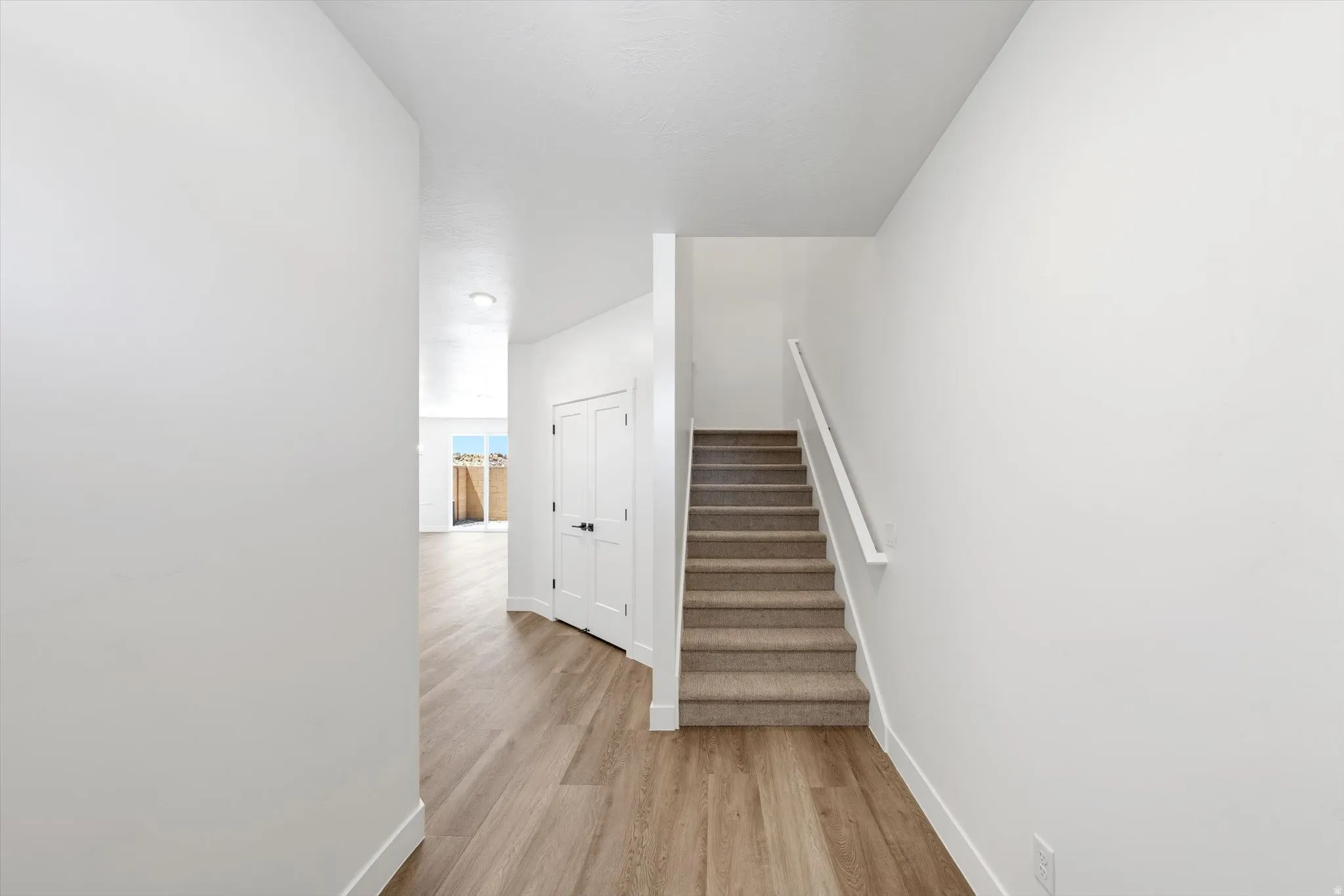 Wood-finish flooring, white baseboards, and a carpeted staircase with a white handrail