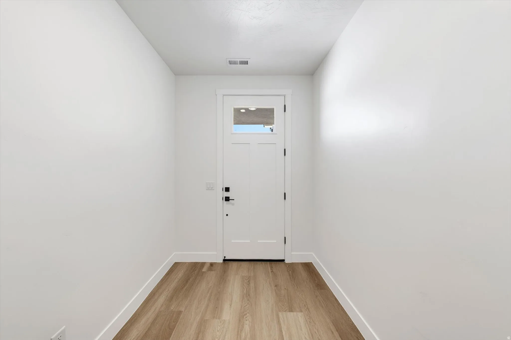 White interior door with glass insert, wood-finish flooring, and white walls