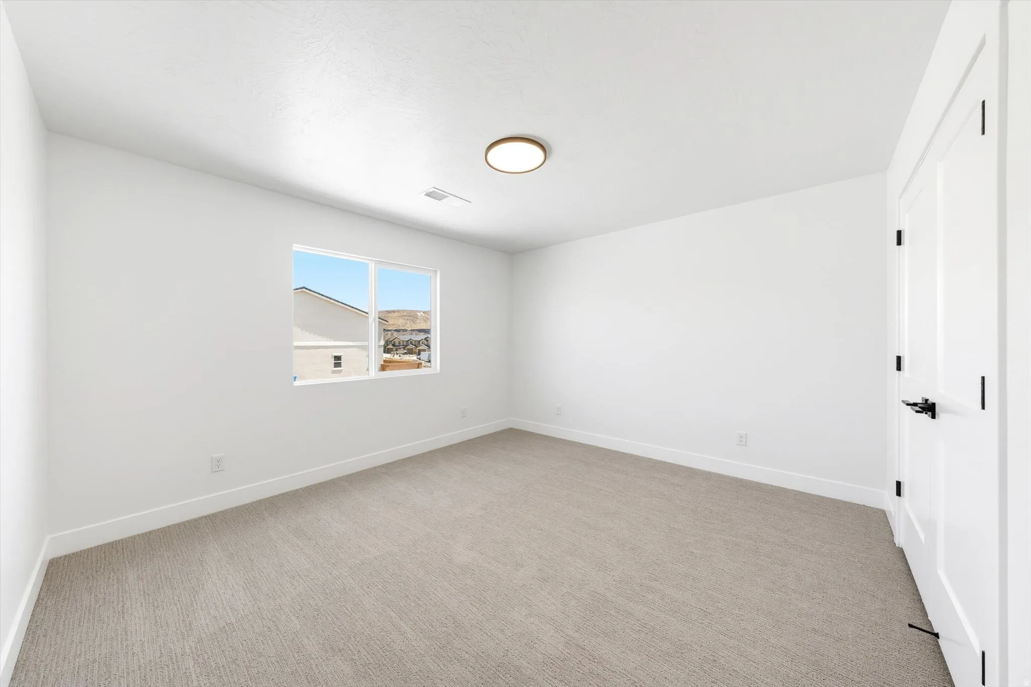 Neutral tone carpet flooring, white painted walls, a flush-mount ceiling light fixture, and a window with a mountain backdrop