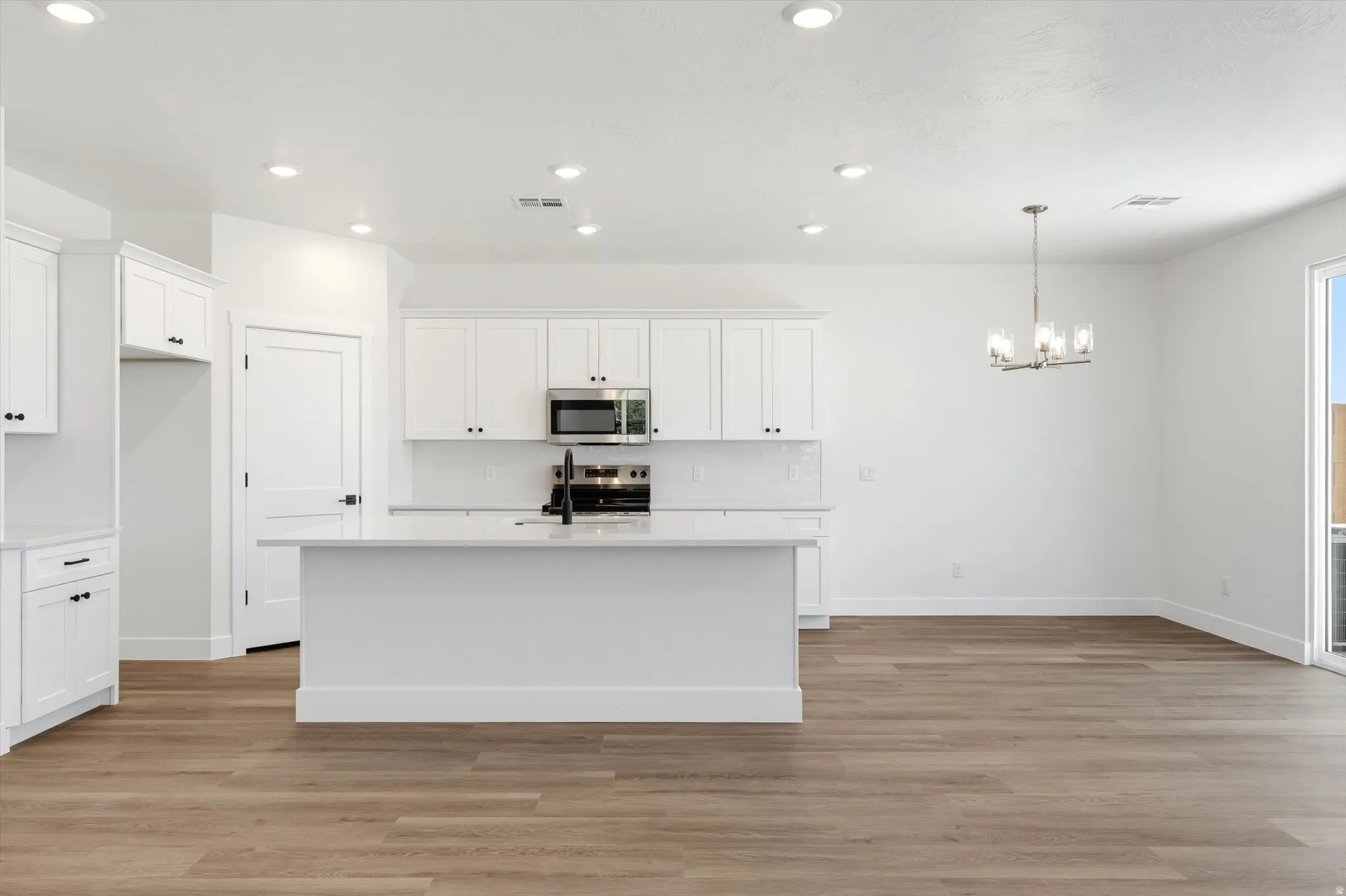 Contemporary kitchen featuring white cabinetry, a central island, stainless steel appliances, and wood-finish flooring