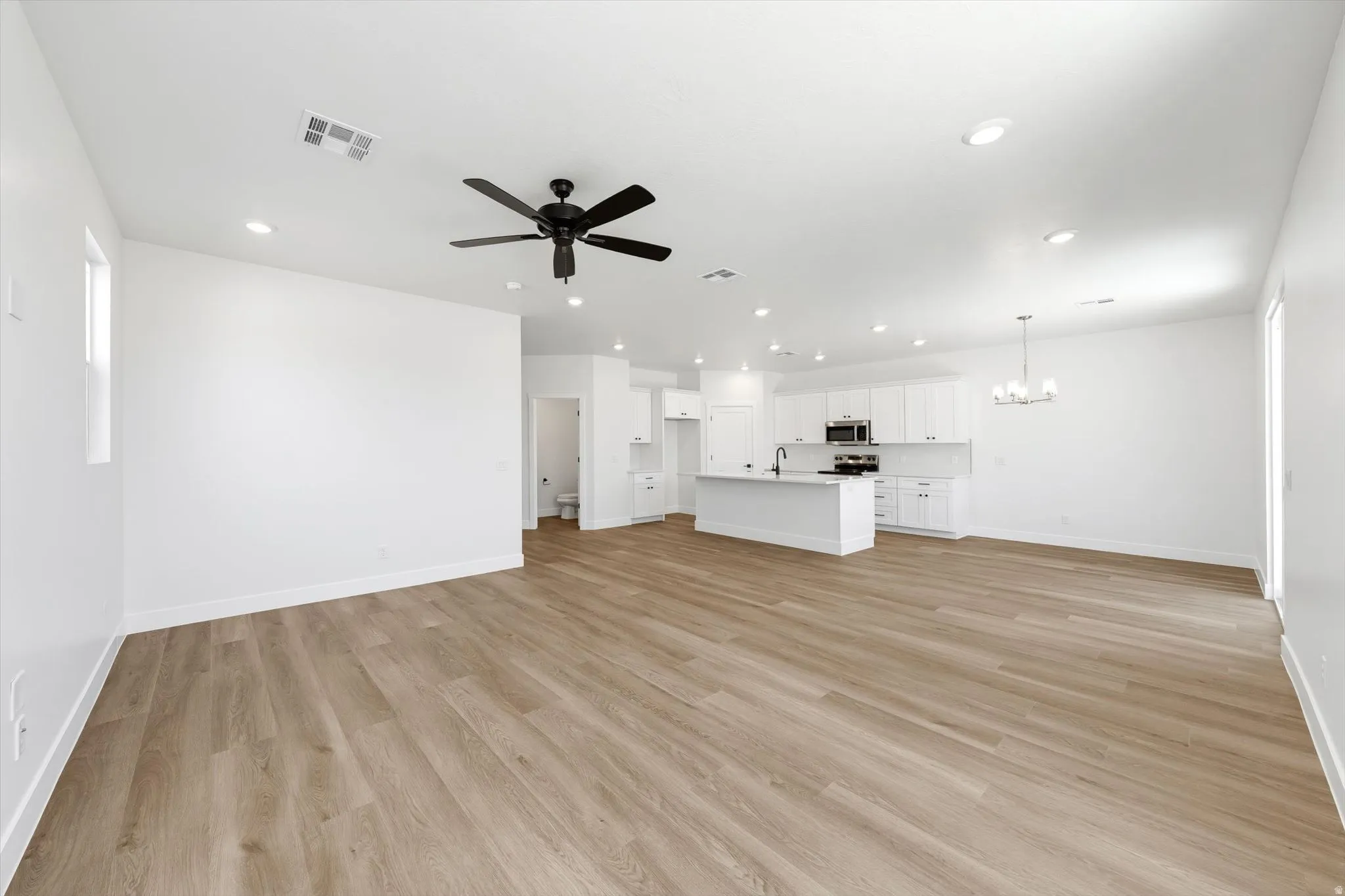 Expansive open-concept living area with wood-finish flooring, recessed lighting, and a ceiling fan
