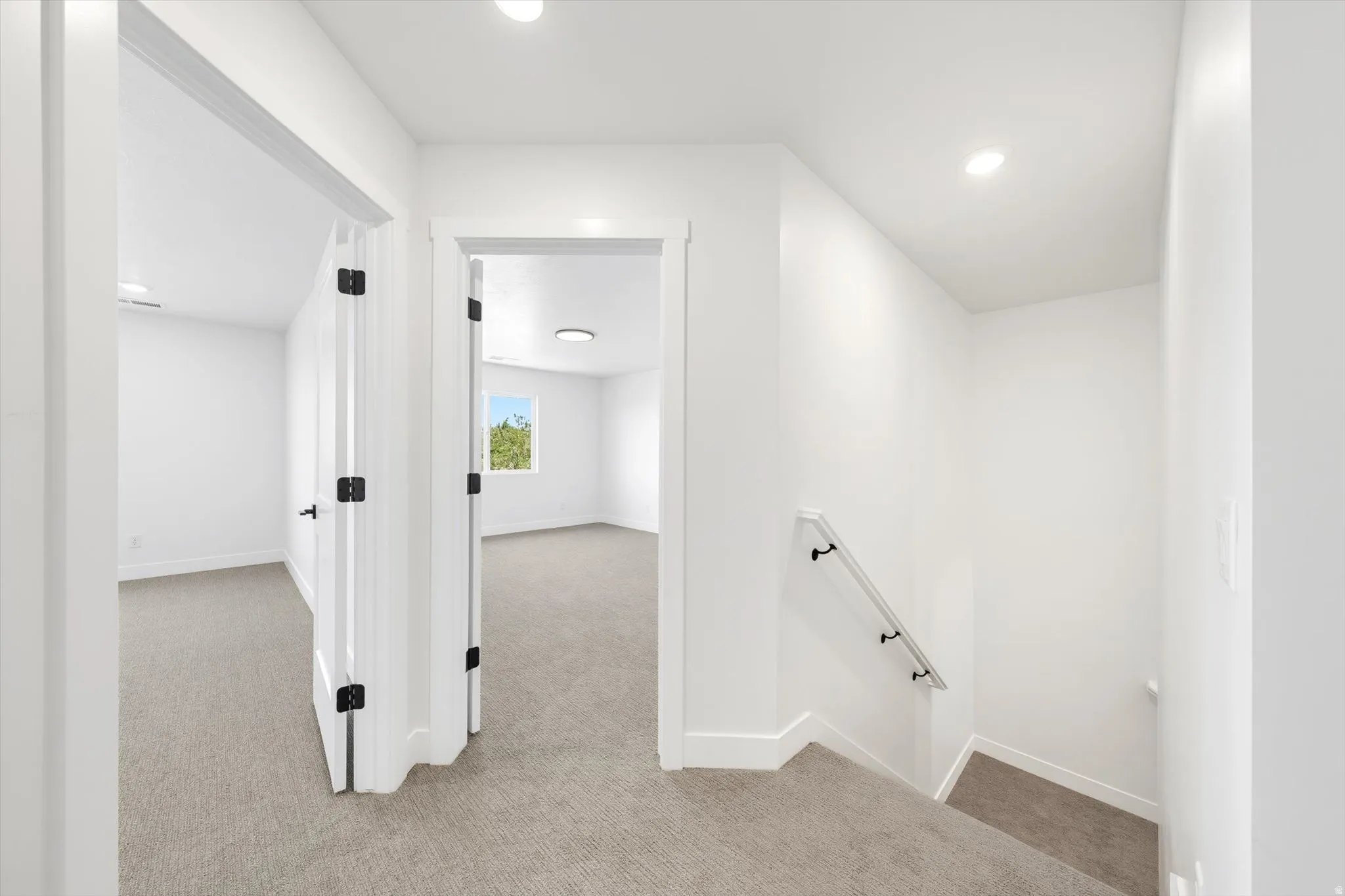 White walls with recessed lighting, carpeted flooring, white doors with matte black hardware, and a staircase with a handrail