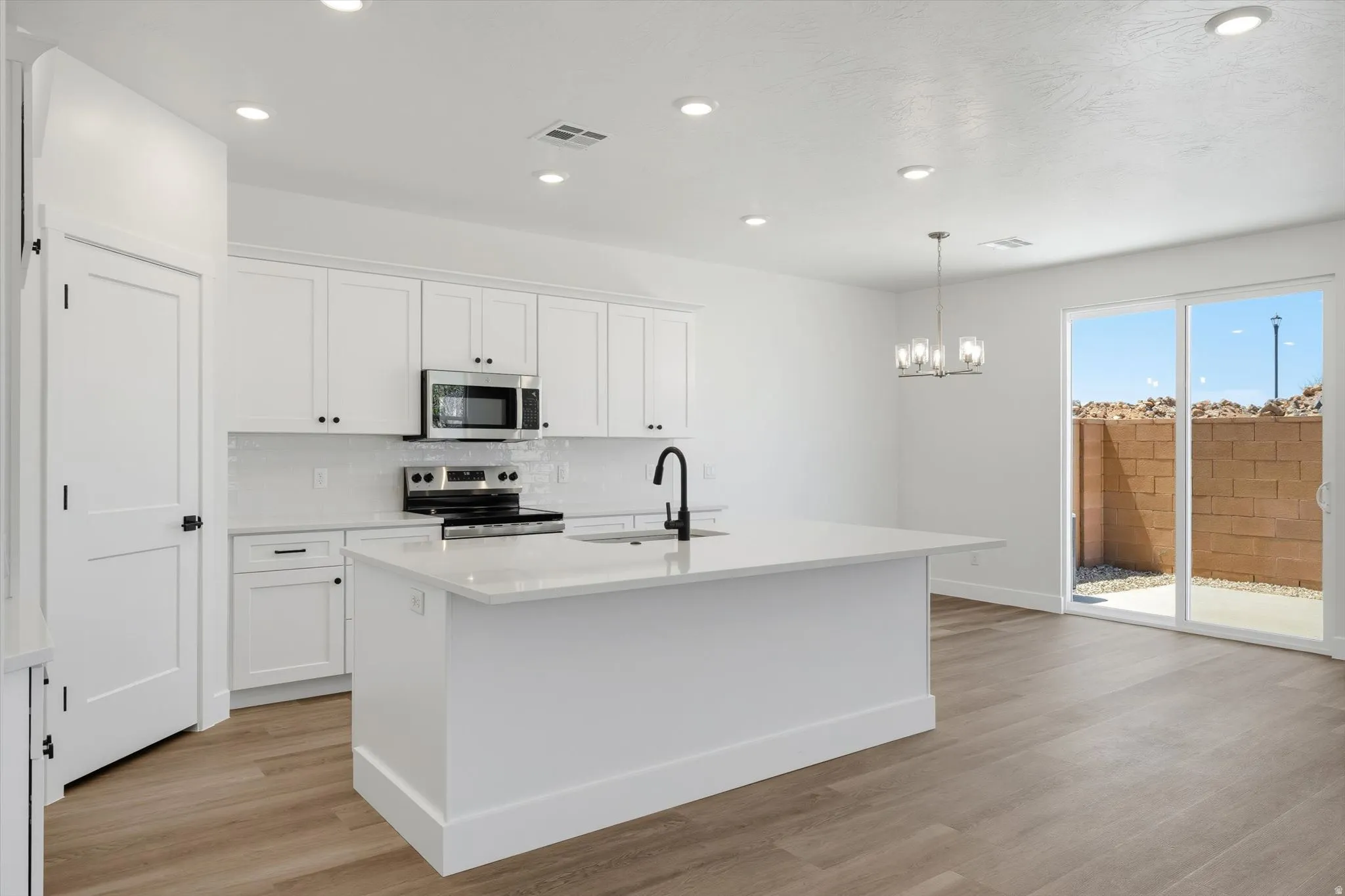 Kitchen featuring white cabinetry, a large central island with a solid surface countertop, stainless steel appliances, and wood-finish flooring
