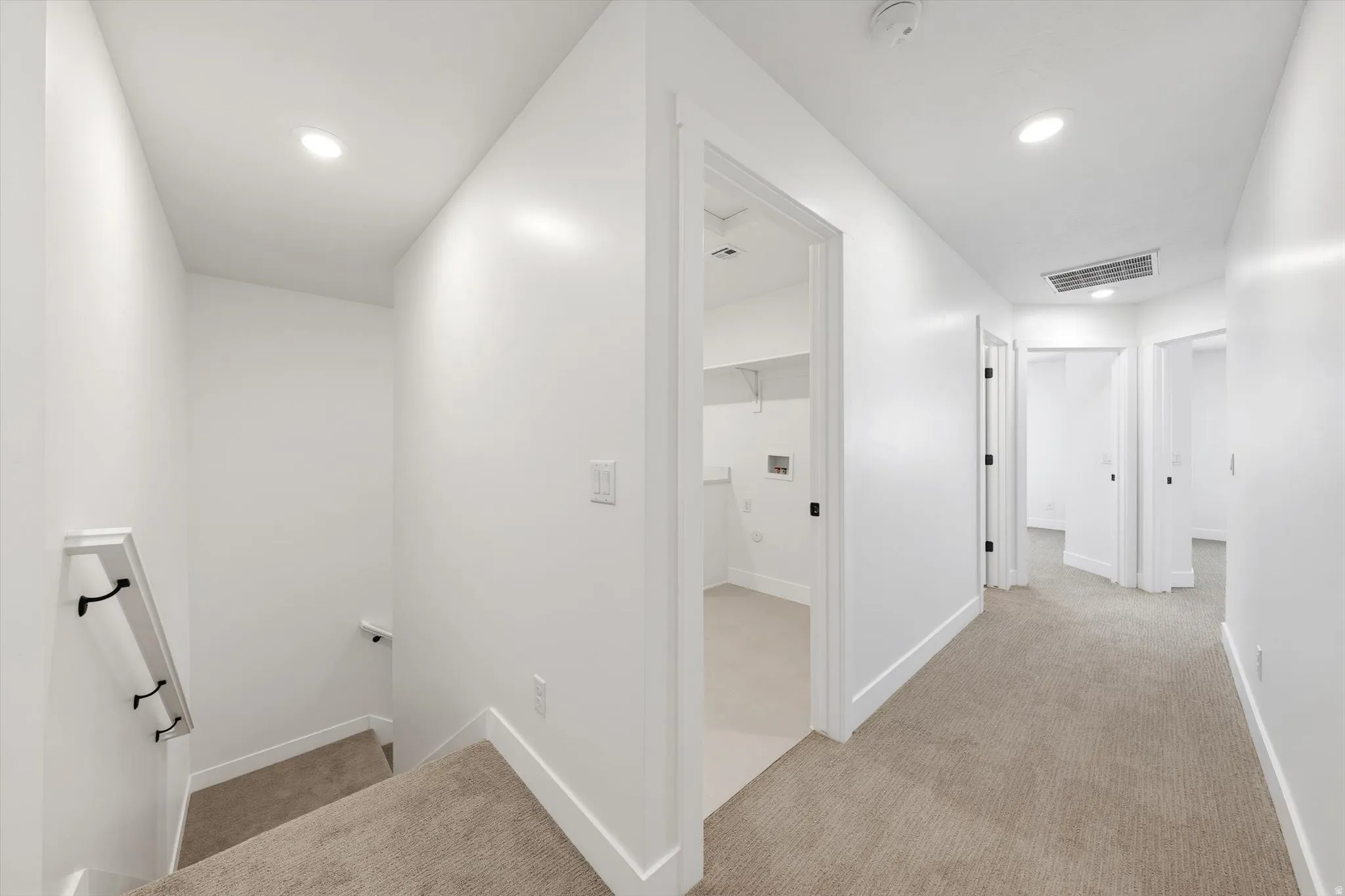 Hallway with recessed lighting, carpet flooring, multiple doorways, and a laundry area with shelving