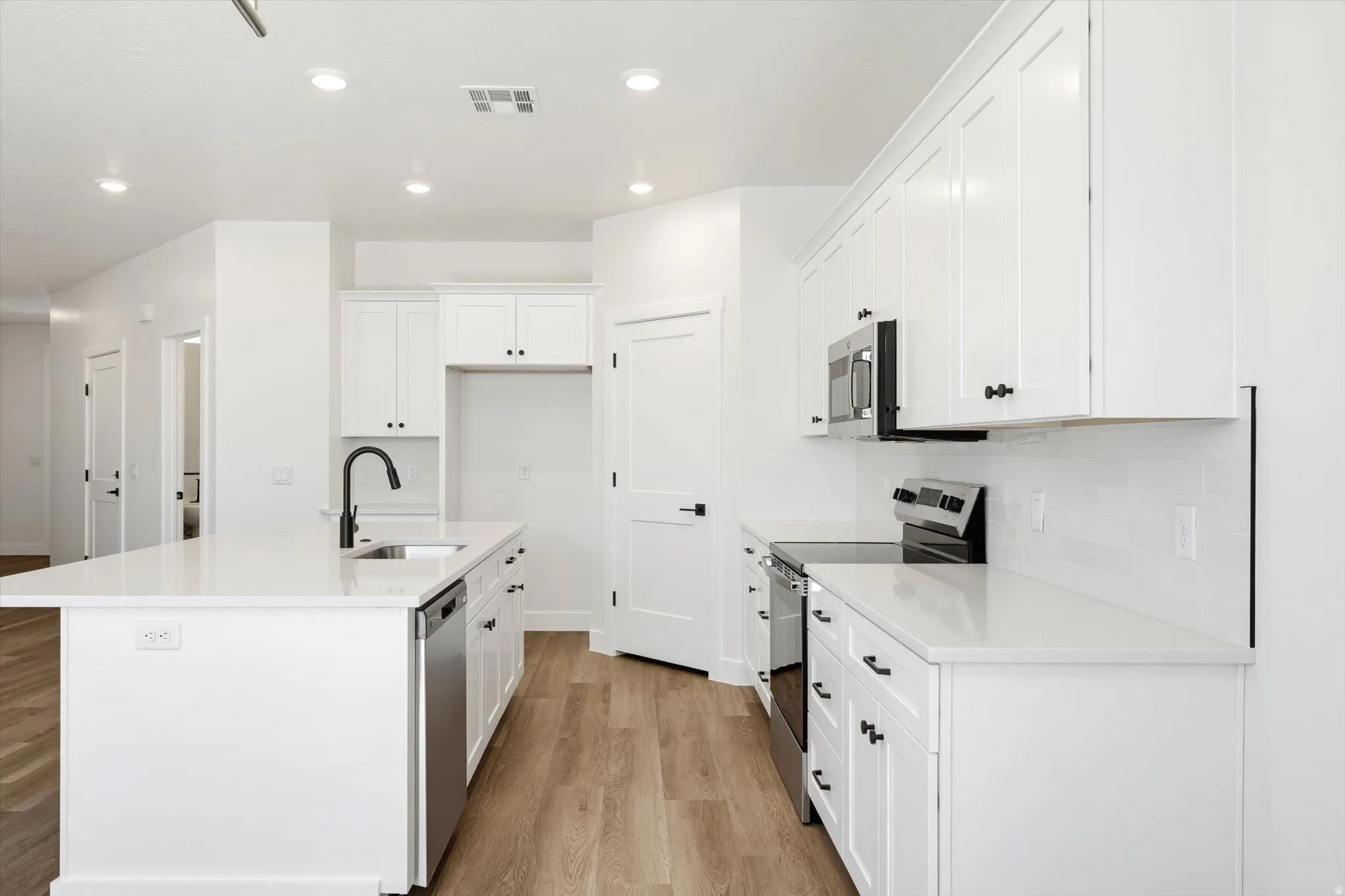 Kitchen featuring white shaker cabinetry, stainless steel appliances, a center island with sink, quartz countertops, and wood-finish flooring