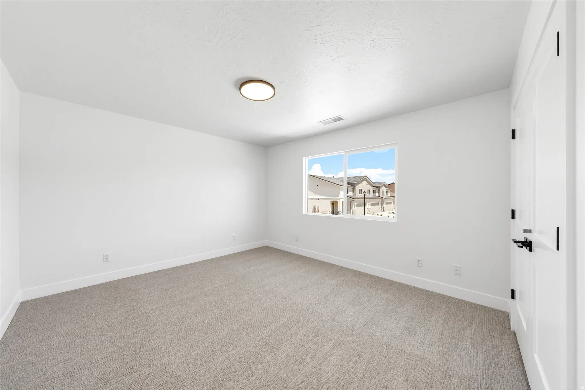 Neutral carpeting, white painted walls, white trim, recessed window with exterior scenery, and a ceiling-mounted light fixture