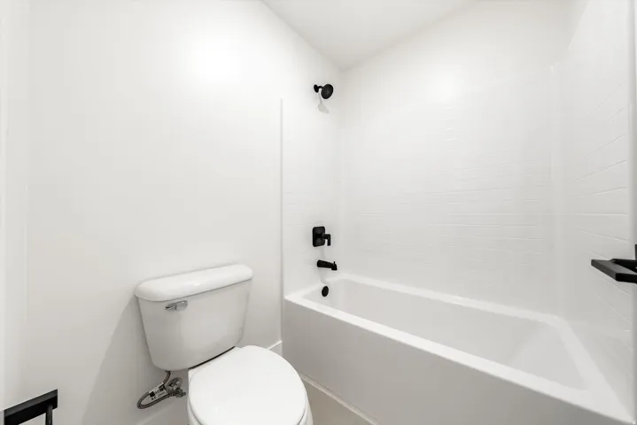 White subway tile tub surround, matte black fixtures, and a white toilet