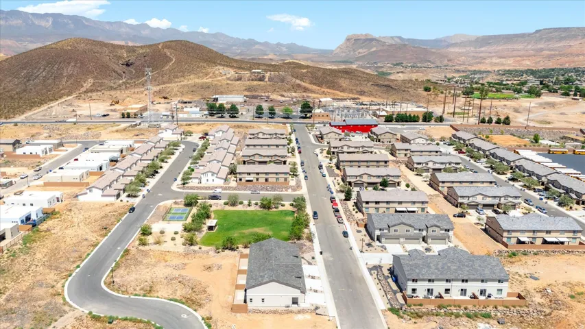 Community setting featuring a paved road network, uniform residential structures, a central green space, and a tennis court