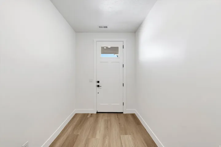 White interior door with glass insert, wood-finish flooring, and white walls