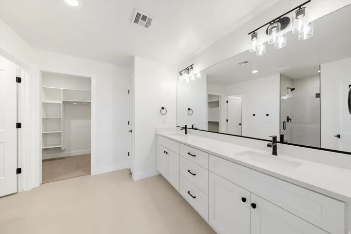 Dual vanity with white cabinetry and integrated sinks, matte black hardware, large wall-mounted mirror, and overhead linear lighting