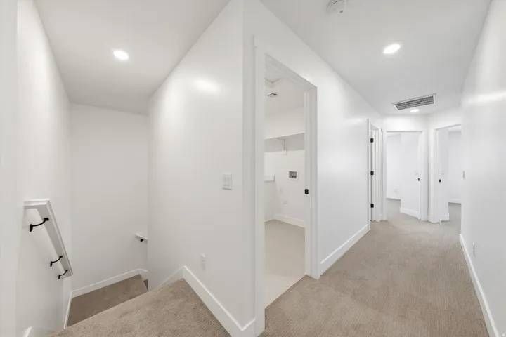 Hallway with recessed lighting, carpet flooring, multiple doorways, and a laundry area with shelving
