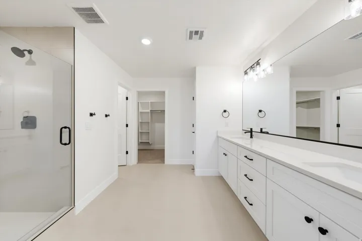 Spacious bathroom featuring a glass-enclosed shower, dual vanity with white cabinetry, light-colored flooring, and a large mirror with overhead lighting