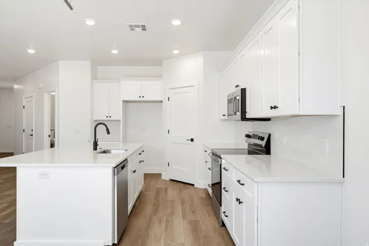 Kitchen featuring white shaker cabinetry, stainless steel appliances, a center island with sink, quartz countertops, and wood-finish flooring