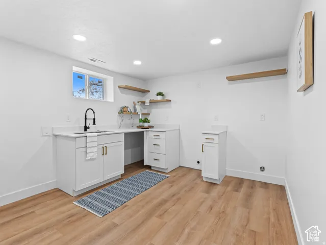 Contemporary utility space featuring wood-finish flooring, white cabinetry, a sink with a matte black faucet, and recessed lighting