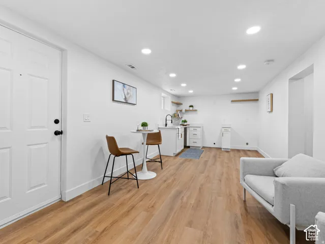 Wood-finish flooring throughout, recessed lighting, white cabinetry, integrated sink with matte black faucet, and floating shelves
