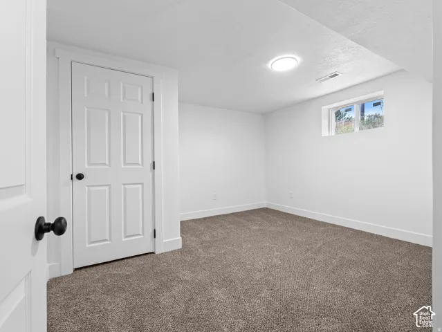 Neutral wall paint with textured carpet flooring, white trim, and a window providing natural light