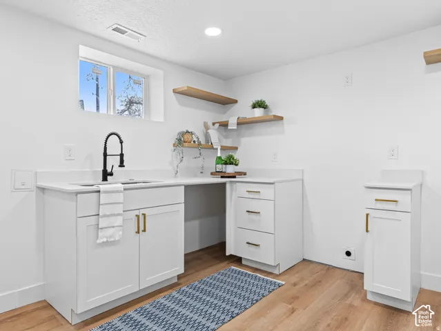 White cabinetry with gold-tone hardware, white countertops, a black gooseneck faucet, light wood-finish flooring, and open shelving