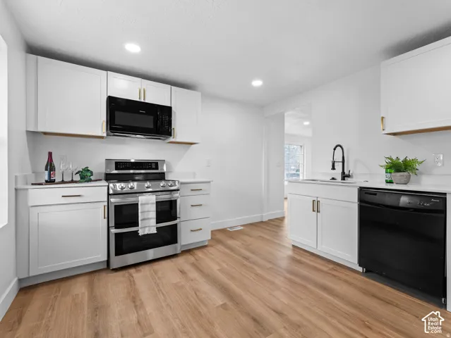 White cabinetry, light-toned wood-finish flooring, stainless steel range, white countertops, and a black microwave